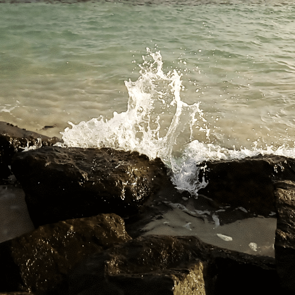 A small wave breaking against the rocks at the Barbados Boardwalk.