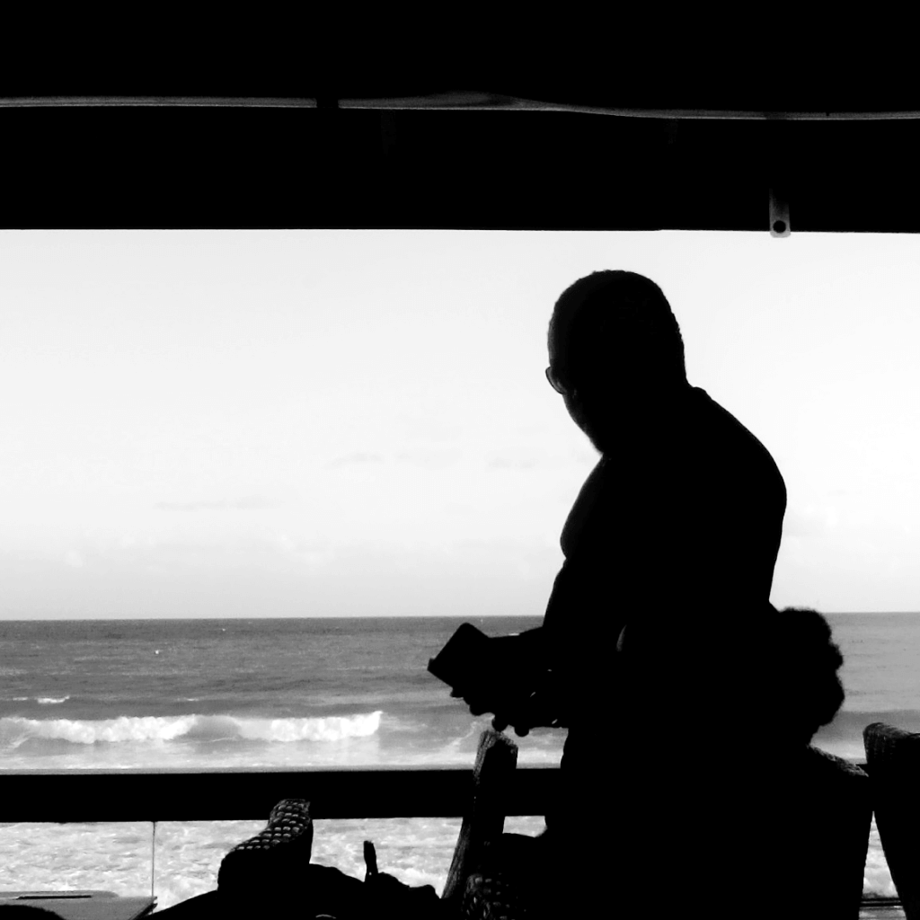 A silhoutte of a man wearing shade against an ocean backdrop.