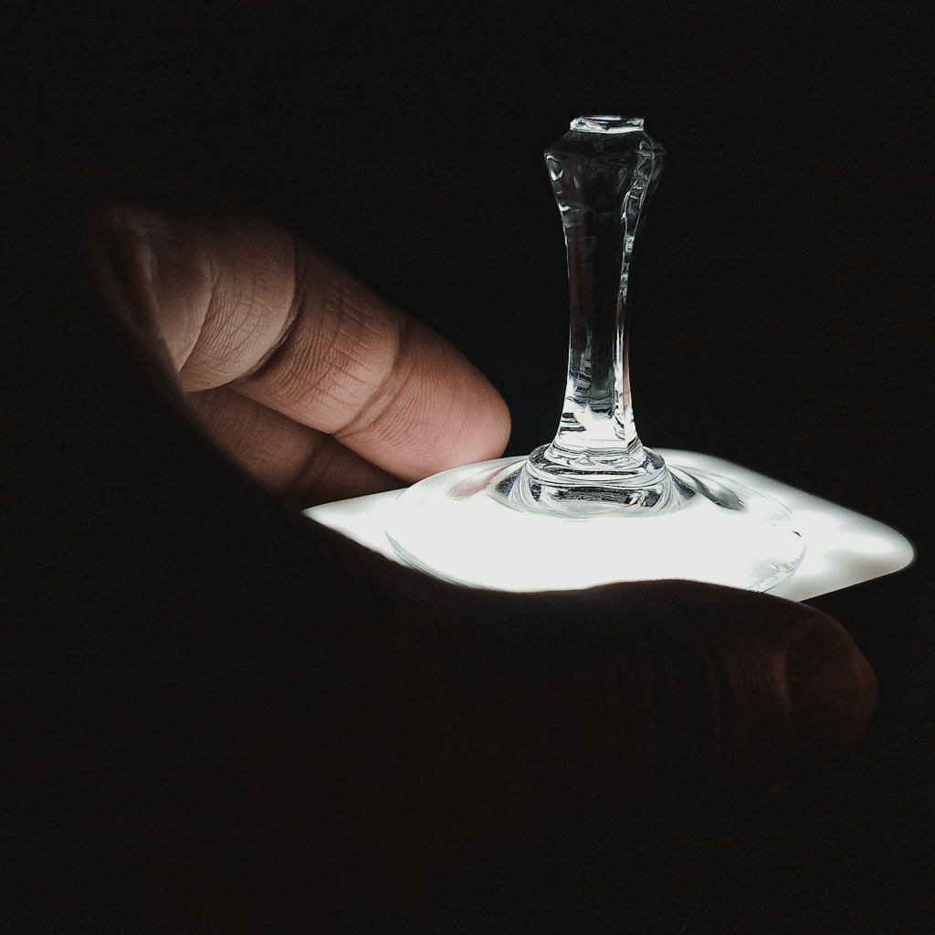 A hand holding on to a LED lamp with a the base of a broken glass wine sitting on top.